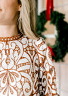 Close up of ladder trim at round neck and cream and reddish-brown lacework over an ivory lining. 