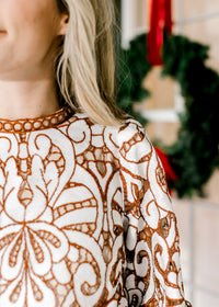 Close up of ladder trim at round neck and cream and reddish-brown lacework over an ivory lining. 