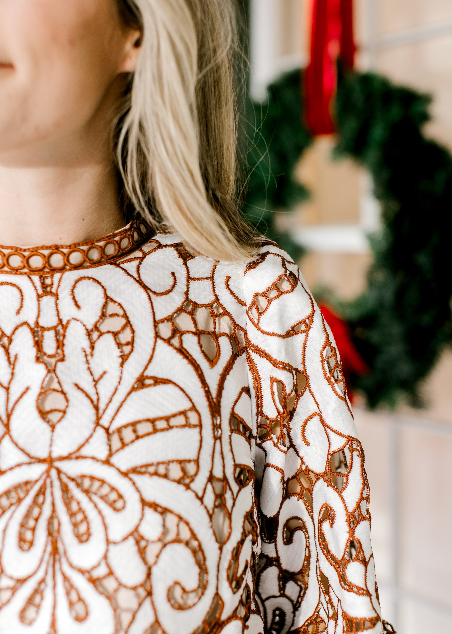 Close up of ladder trim at round neck and cream and reddish-brown lacework over an ivory lining. 