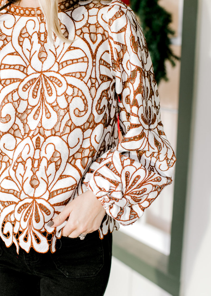 Close up of brown and cream lacework over an ivory lining with long sleeves and a round neck. 