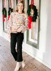 Model wearing black jeans and booties with a cream and reddish-brown lacework top with long sleeves.