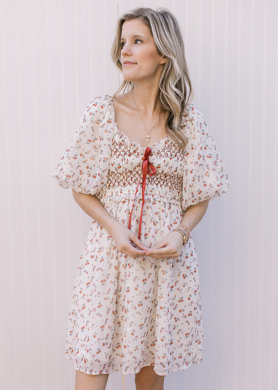 Model wearing a cream knee length dress  with red cherry print and embroidered cream floral detail. 
