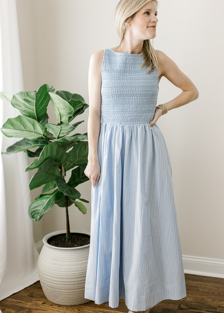 Model wearing a soft blue sleeveless maxi with white pinstripes, smocked bodice and a round neck. 