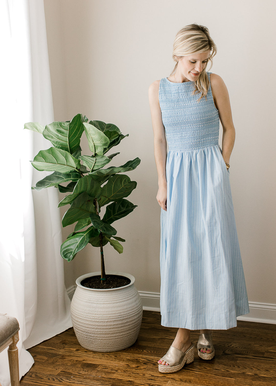 Model wearing heels and a soft blue sleeveless maxi with white pinstripes, smocked bodice. 