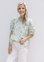 Model wearing a sage babydoll top with cream daisies, lined with puff short sleeves. 