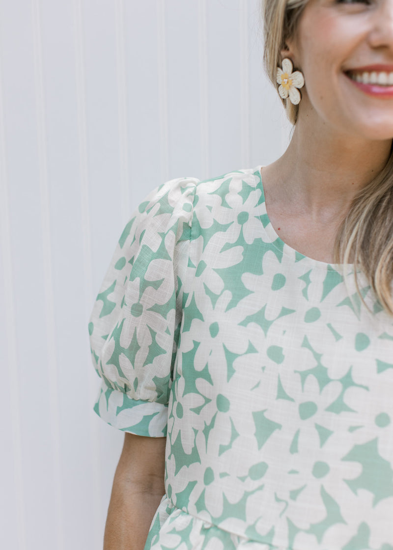 Close up of puff short sleeves and a round neck on a sage top with cream daisies. 