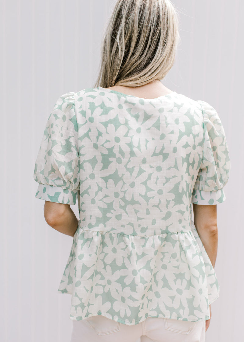 Back view of Model wearing a sage babydoll top with cream daisies, lined with puff short sleeves.