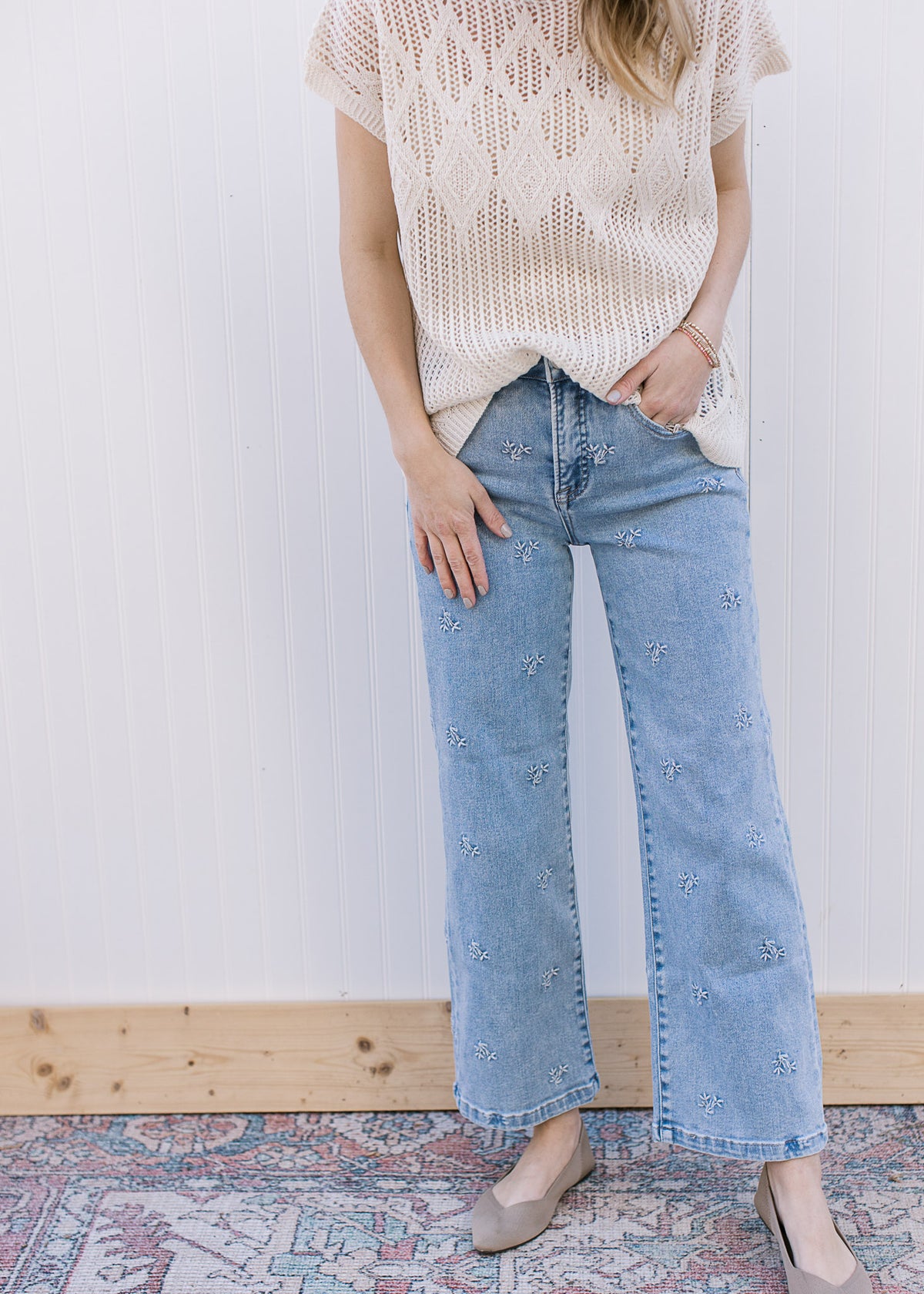 Model wearing light wash jeans with daisy embroidery, slightly cropped fit and wider leg. 