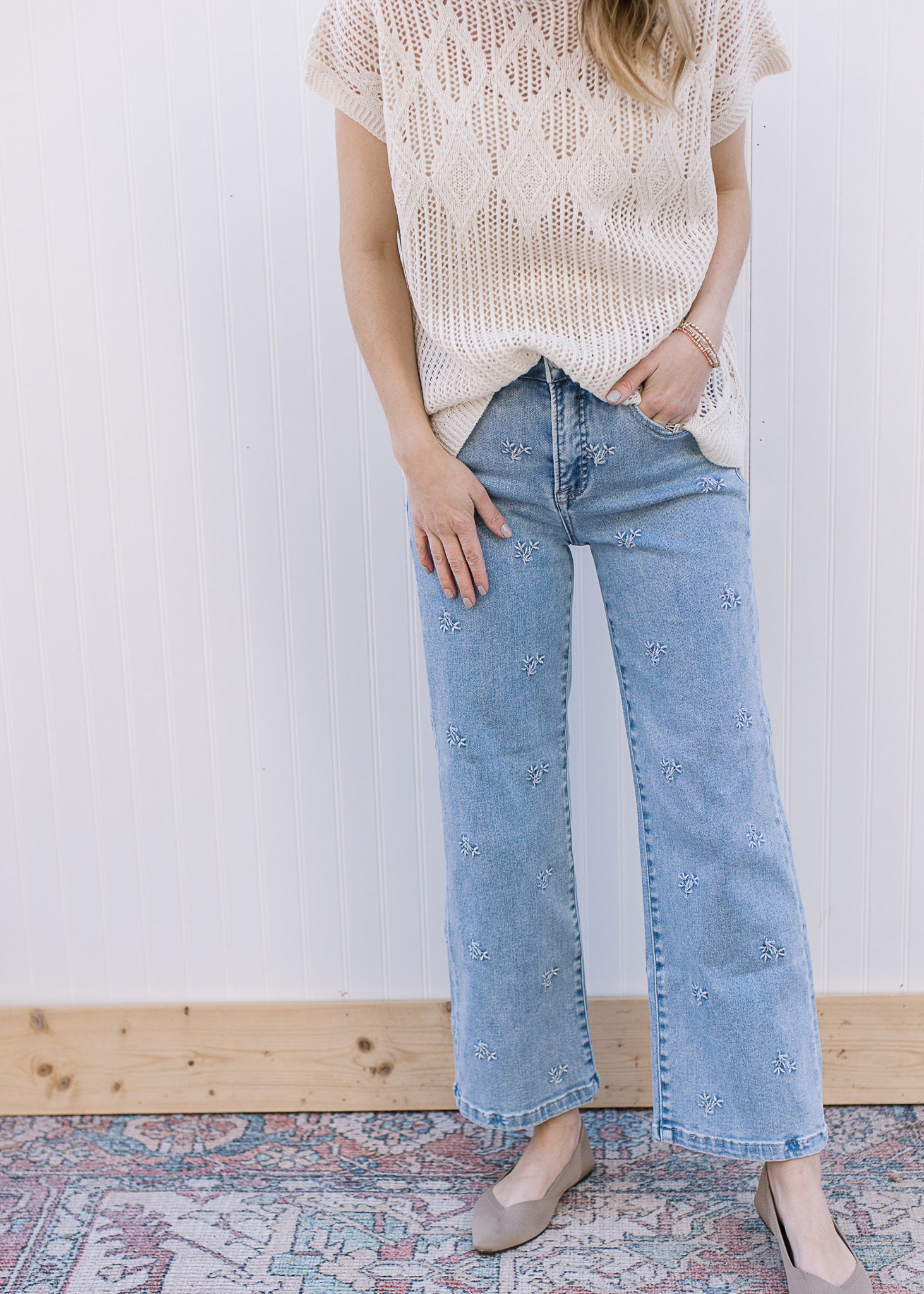 Model wearing light wash jeans with daisy embroidery, slightly cropped fit and wider leg. 