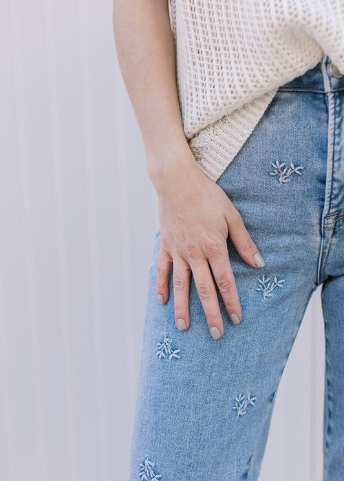 Close up of embroidered daisies on light wash jeans with a slightly cropped fit and wider leg. 