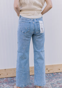 Back view of Model wearing light wash jeans with daisy embroidery and slightly cropped fit.
