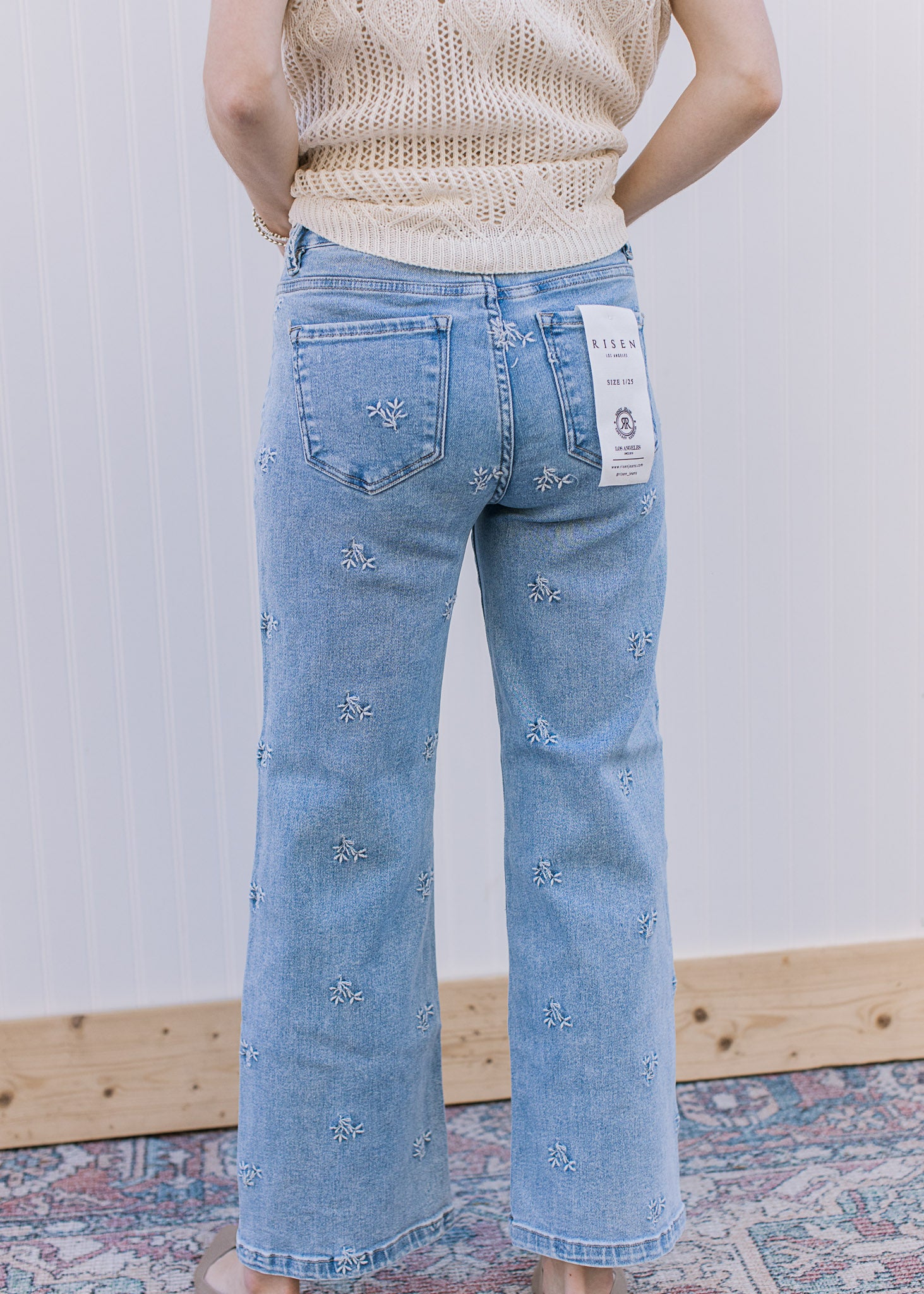 Back view of Model wearing light wash jeans with daisy embroidery and slightly cropped fit.