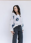 Model wearing an ivory v-neck sweater with navy flowers, exposed hem and long sleeves. 