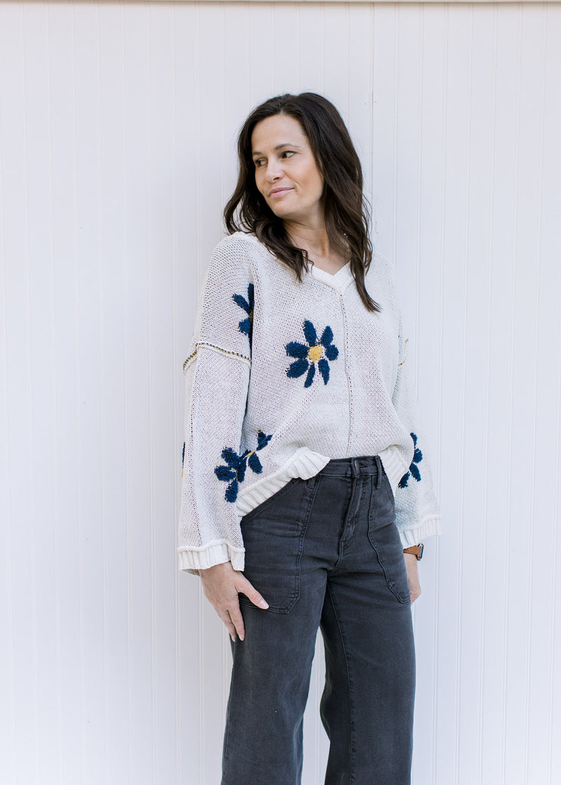 Model wearing an ivory v-neck sweater with navy flowers, exposed hem and long sleeves. 