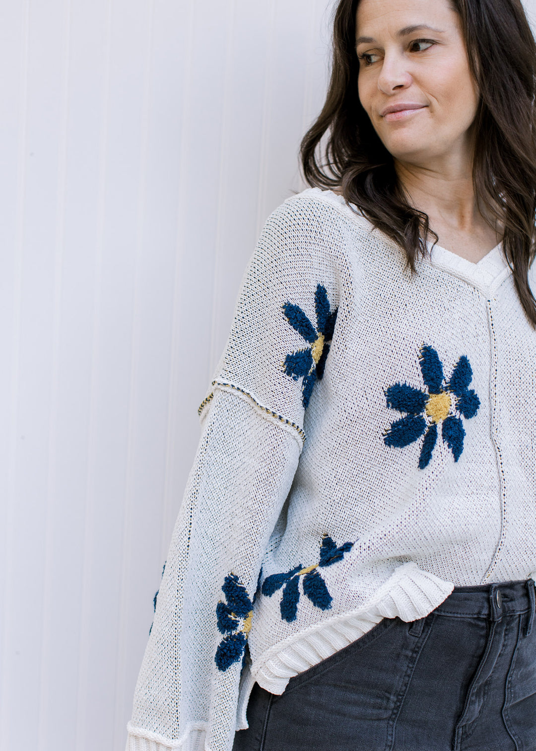 Close up of blue flowers with yellow center on an ivory long sleeve sweater with exposed hem. 