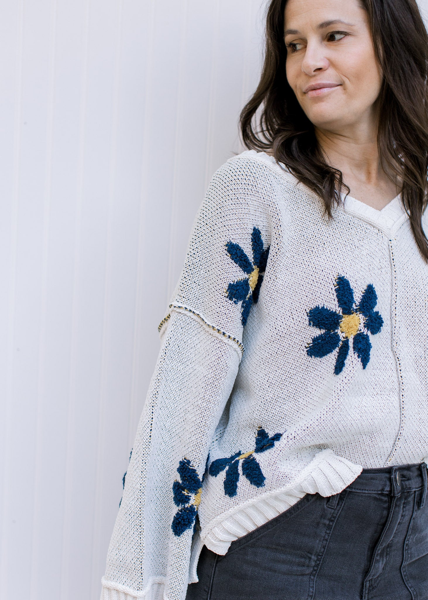 Close up of blue flowers with yellow center on an ivory long sleeve sweater with exposed hem. 