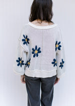 Back view of Model wearing an ivory sweater with navy flowers, exposed hem and long sleeves. 