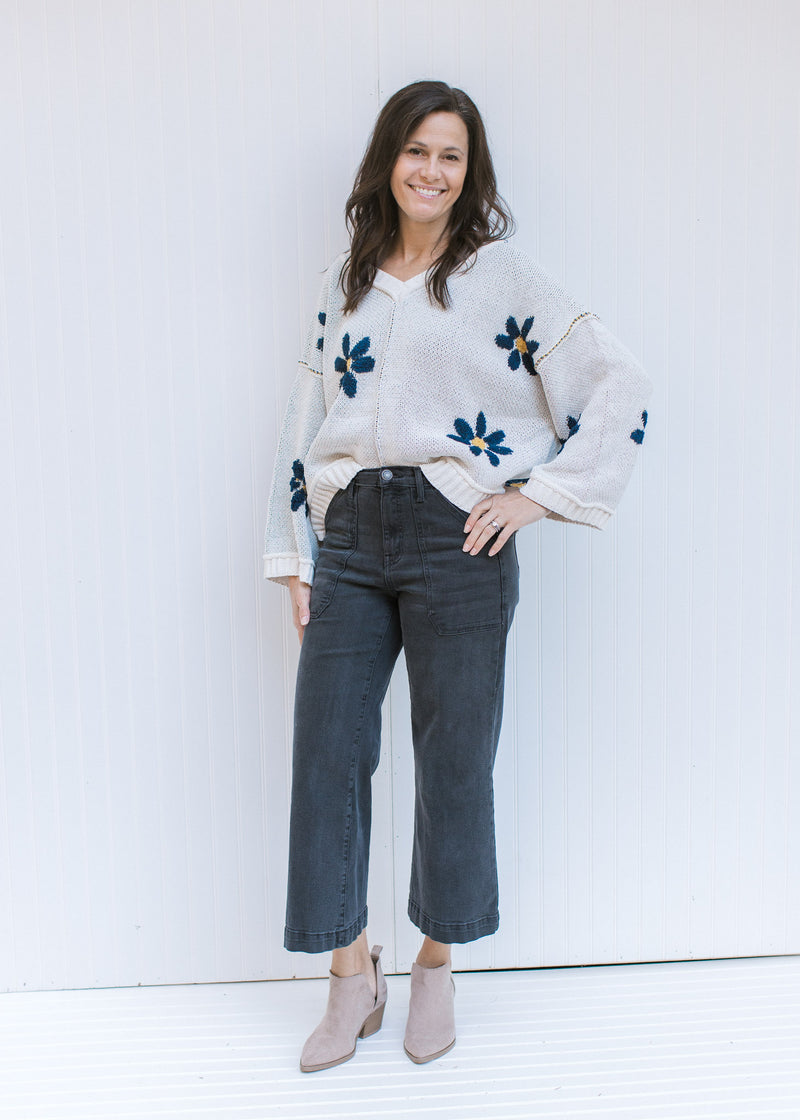 Model wearing jeans, booties and an ivory v-neck sweater with navy flowers and exposed hem. 