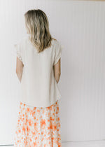 Back view of Model wearing an oatmeal top with a smocked detail at the v-neck and short sleeves.  