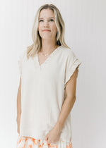 Model wearing an oatmeal top with a smocked detail at the v-neck and short sleeves.  
