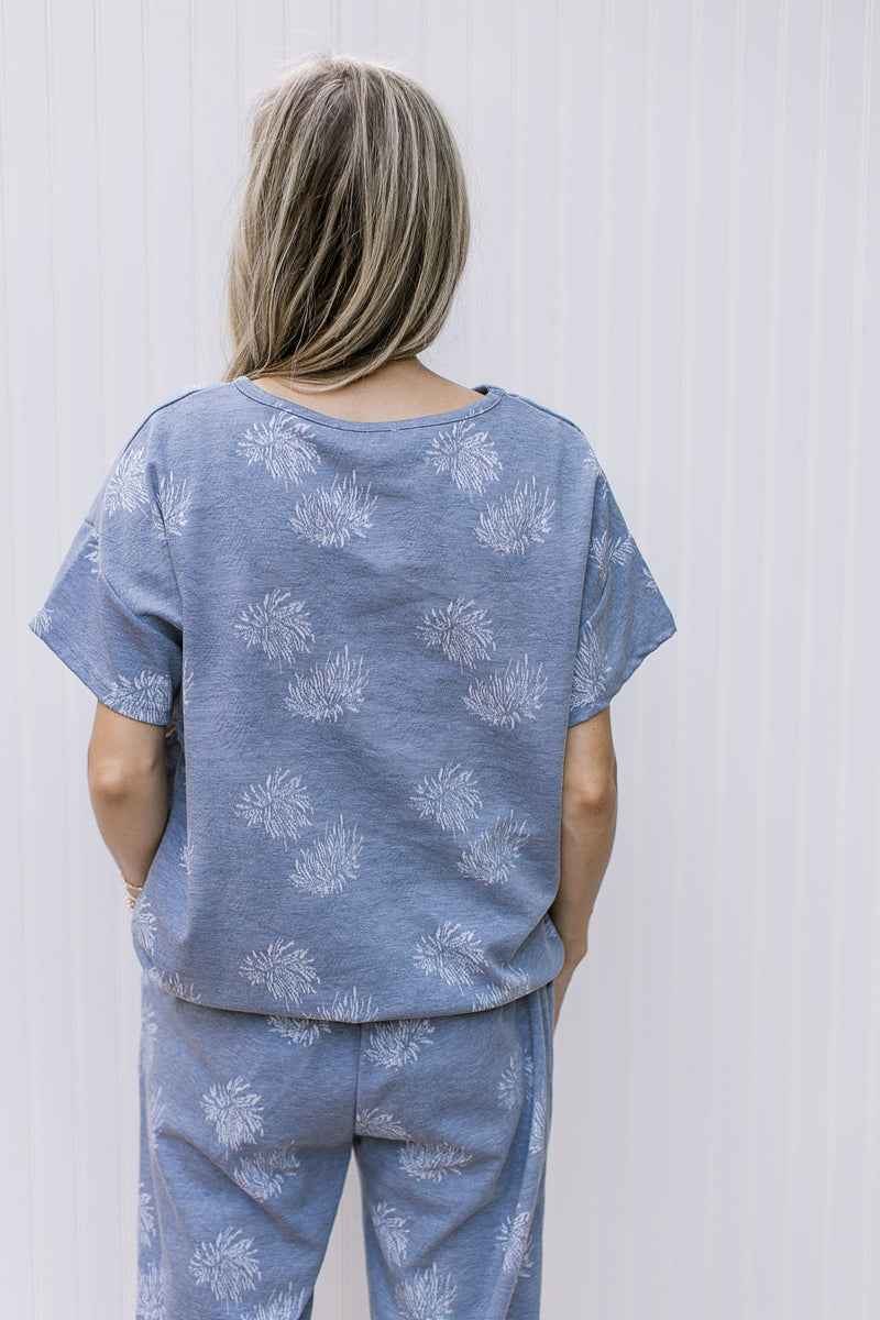 Back view of Model wearing a denim color top with light blue dandelions and short sleeves.