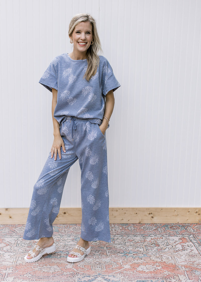 Model wearing denim color top with light blue dandelions and short sleeves.