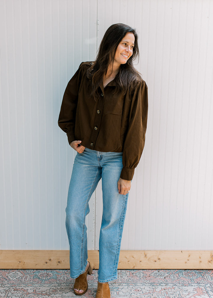 Model wearing a slightly cropped dark brown jacket with buttons and pleated shoulders. 
