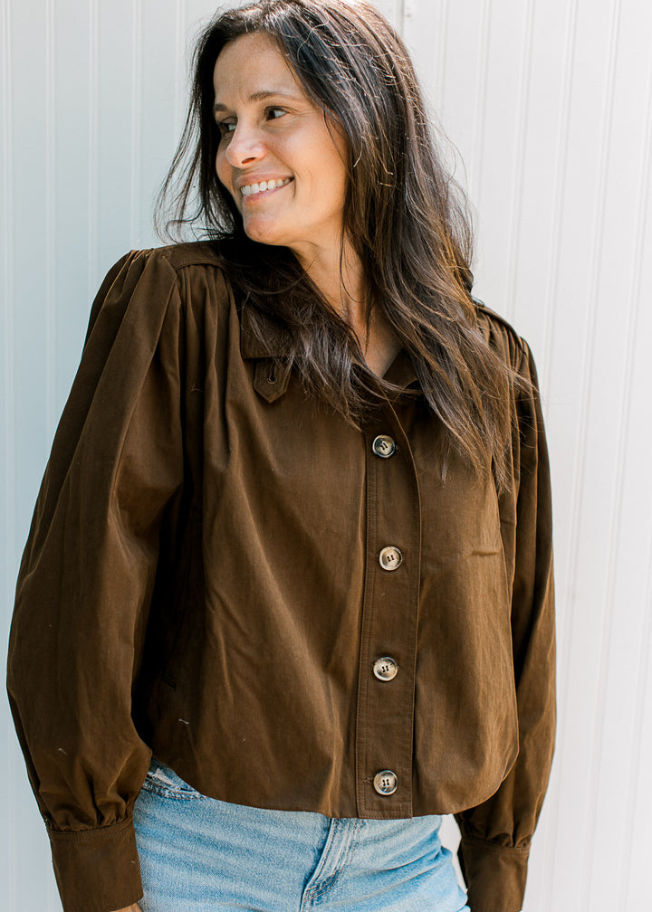 Model wearing dark brown jacket with buttons, pleated shoulders, shoulder pads and long sleeves.