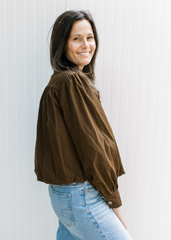 Side view of pleated shoulders and shoulder pads on a dark brown slightly cropped jacket.