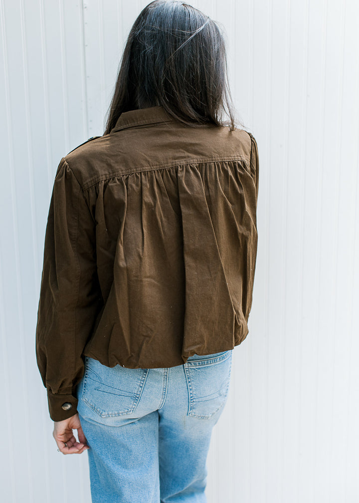 Back view of Model wearing dark brown jacket with slight crop, pleated shoulders and long sleeves.