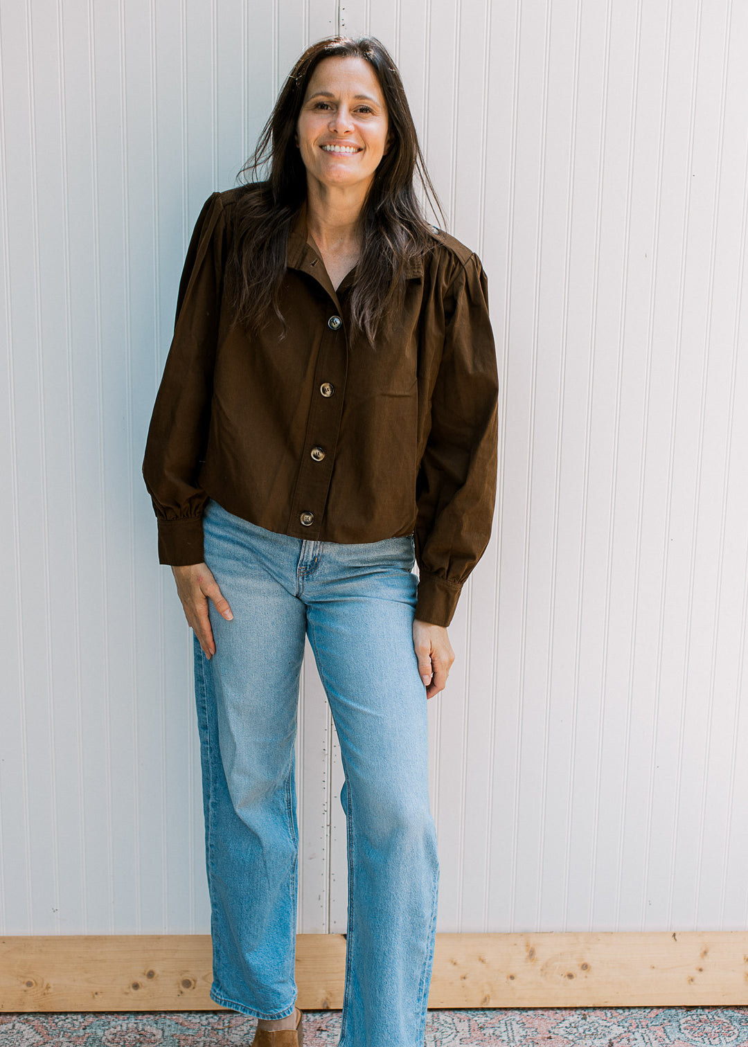 Model wearing jeans and a dark brown, slightly cropped jacket with buttons and long sleeves.