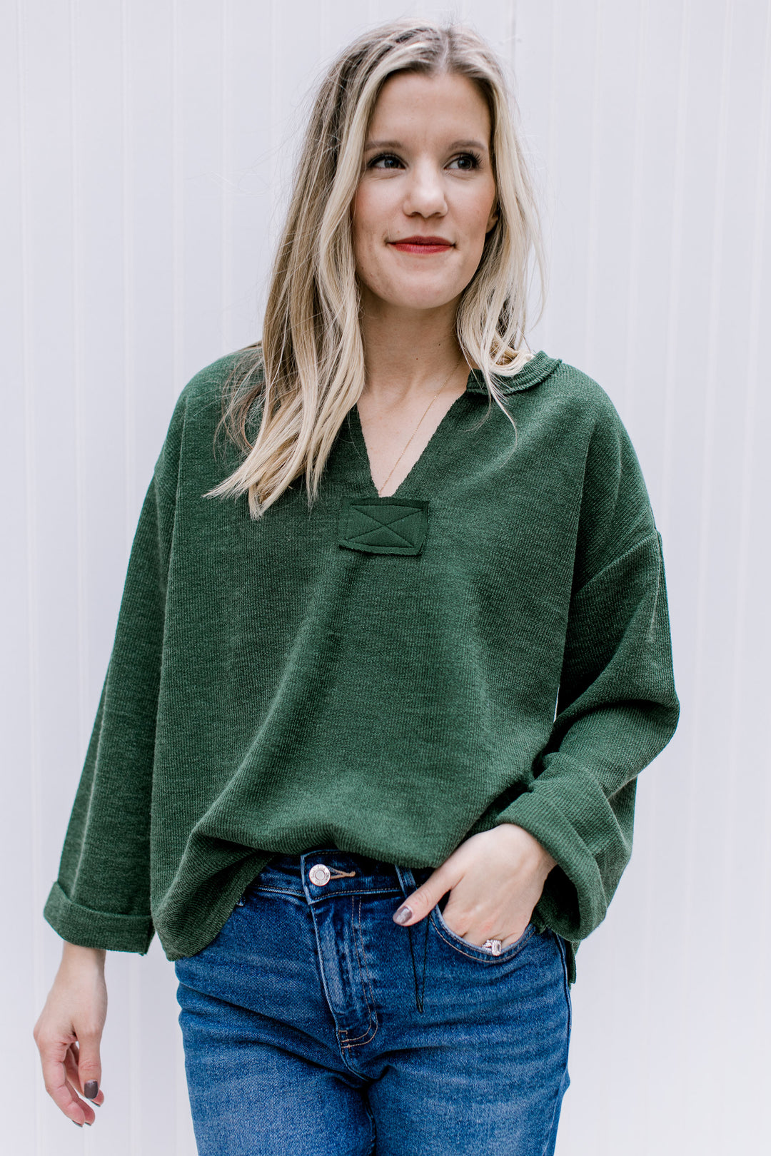 Model wearing a deep olive top with a v-neck and cuffed sleeves. 