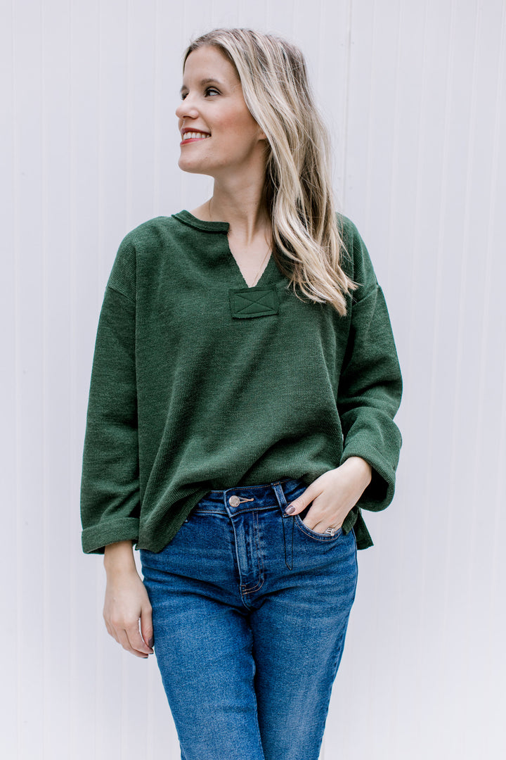Model wearing jeans with a deep olive top with a v-neck and cuffed sleeves.