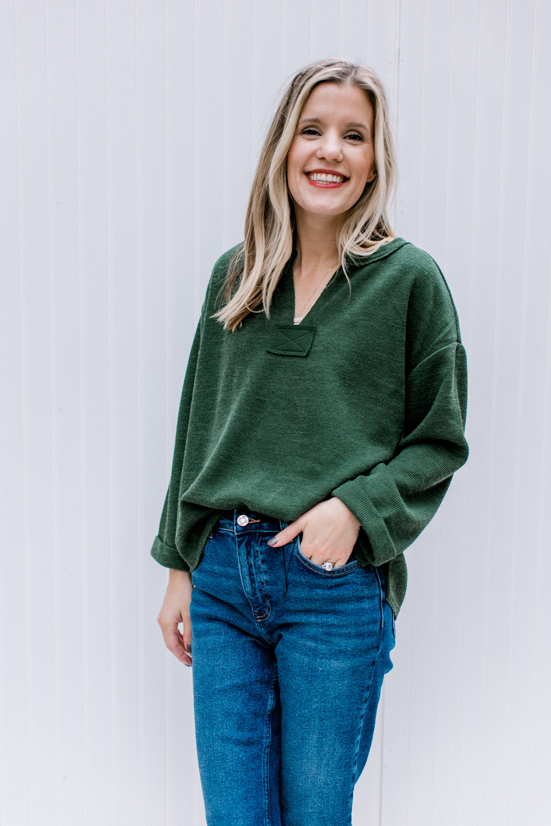 Model wearing a deep olive top with a v-neck, patchwork detail and cuffed sleeves.