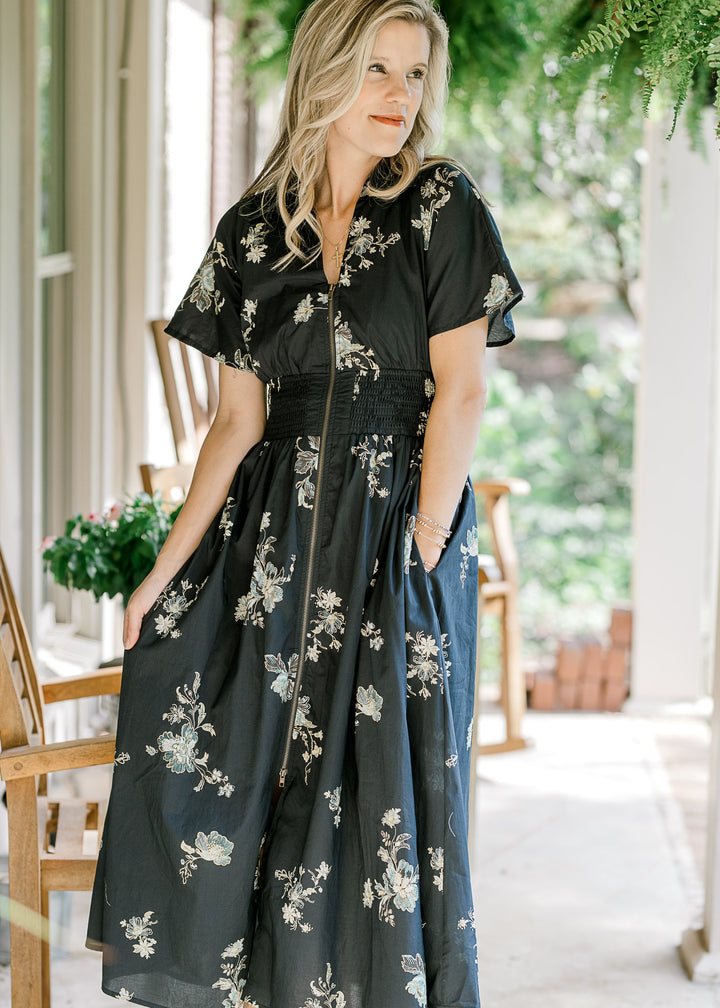 Model wearing a black midi with cream, sage and gold floral, short sleeves and zip front. 