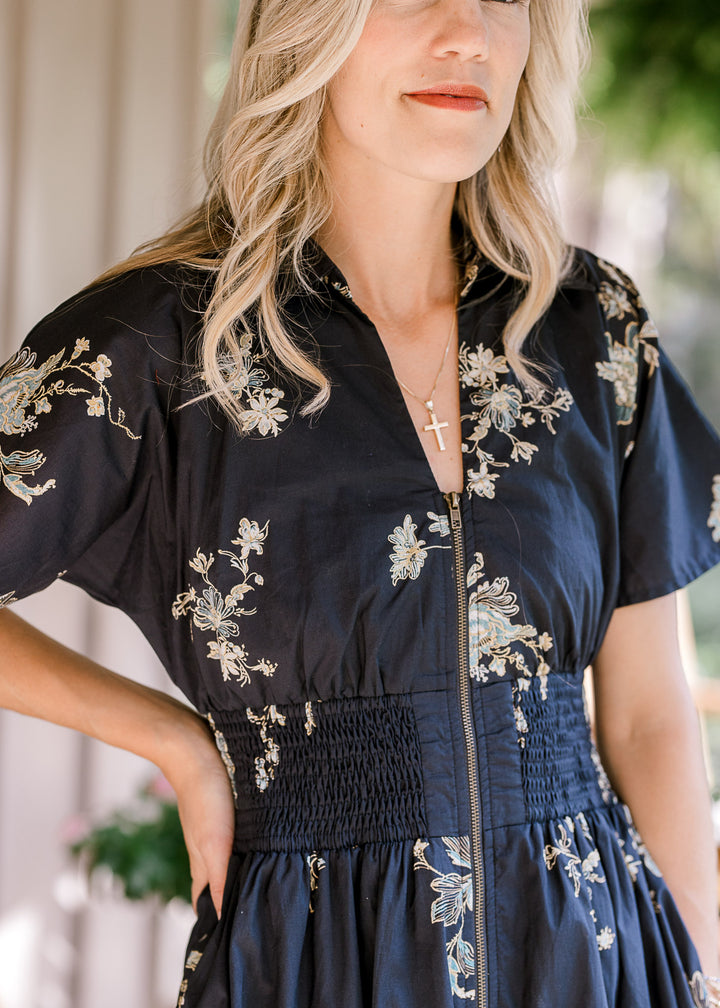 Close up of zipper front, smocked waist and v-neck on a short sleeve black midi with floral. 
