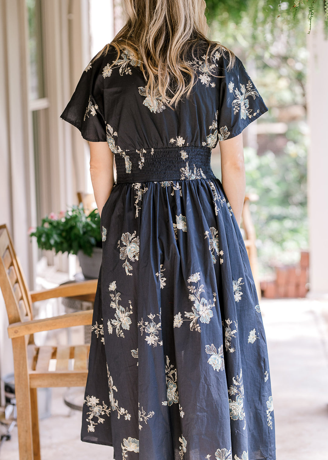 Back view of model wearing a black dress with light color floral, smocked waist and short sleeves. 
