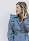 Model wearing a vintage blue coat with a ruffle at the shoulder, button closure and long sleeves. 
