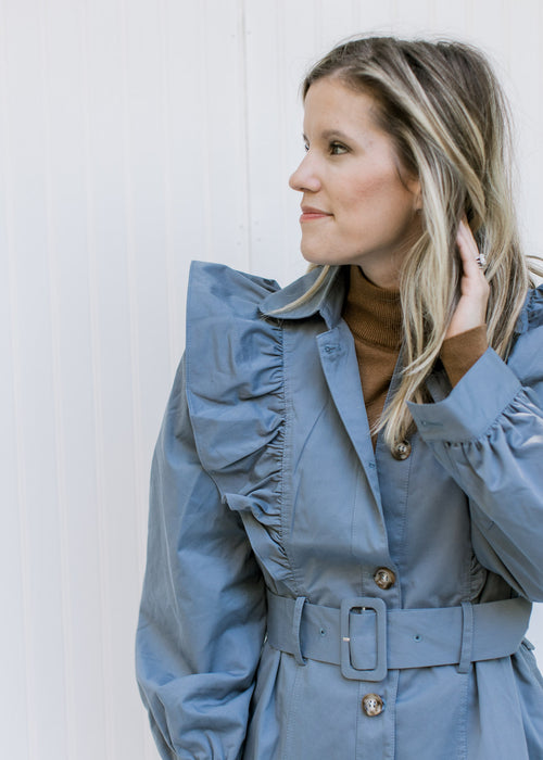 Model wearing a vintage blue coat with a ruffle at the shoulder, button closure and long sleeves. 