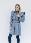 Model wearing jeans with a vintage blue coat with a ruffle at the shoulder and button closure. 