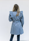 Back view of Model wearing a vintage blue coat with a ruffle at the shoulder and button closure. 