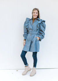 Model wearing jeans and booties with a vintage blue coat with a ruffle at the shoulder and a belt. 