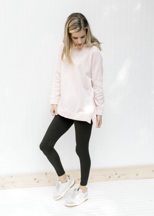 Model wearing black leggings with a blush colored hoodie with long sleeves and a side zippers. 