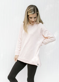 Model wearing black leggings and a blush colored hoodie with long sleeves and two side zippers. 