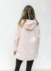 Back view of hoodie on a blush colored sweatshirt with long sleeves and side zippers. 