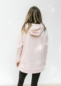 Back view of hoodie on a blush colored sweatshirt with long sleeves and side zippers. 