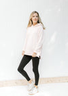 Model wearing black leggings and sneakers with a blush colored hoodie with long sleeves. 