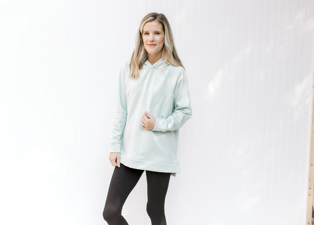 Model wearing black leggings with a mint colored hoodie with long sleeves and a side zippers. 