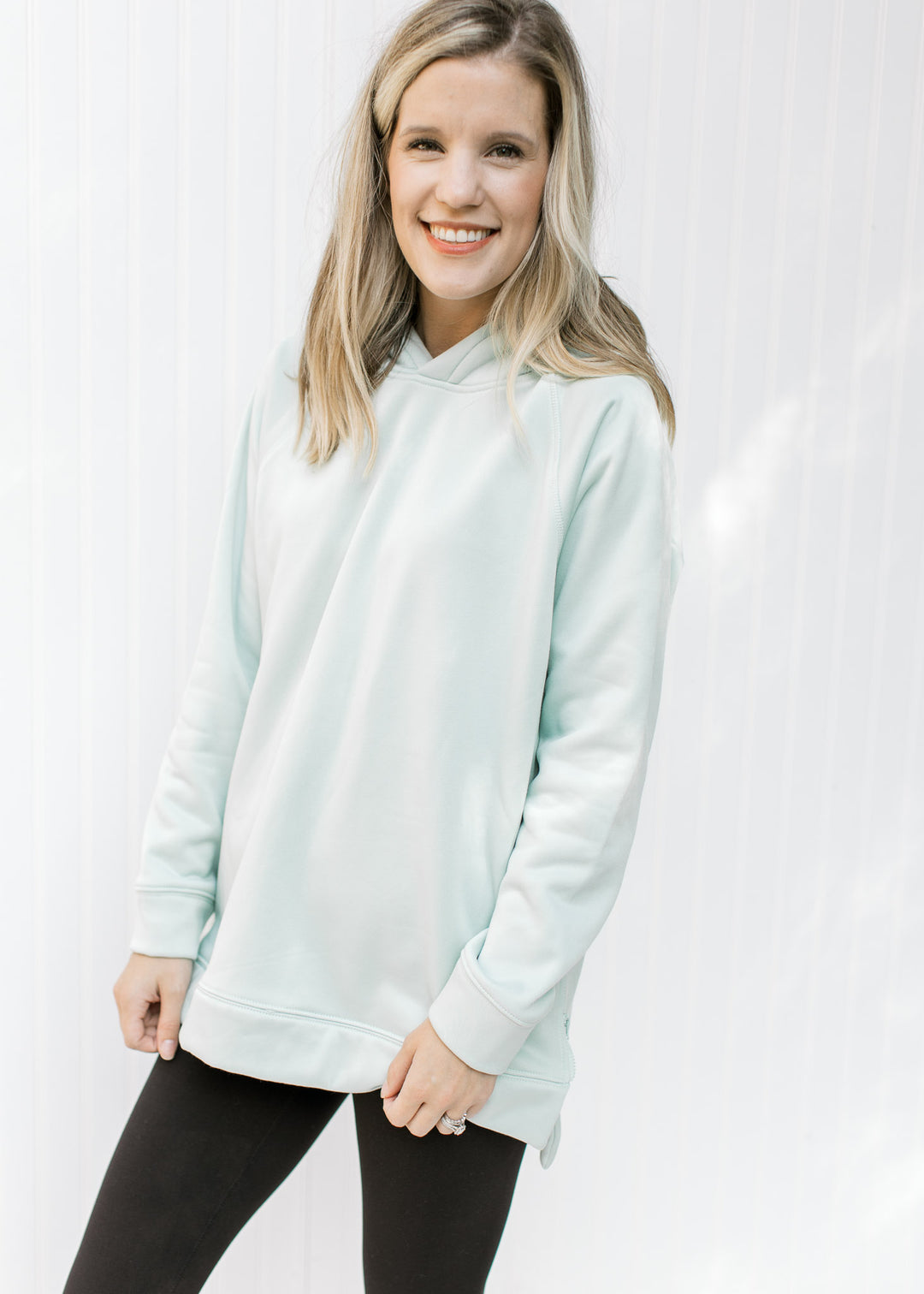 Model wearing a mint colored hoodie with long sleeves and two side zippers. 