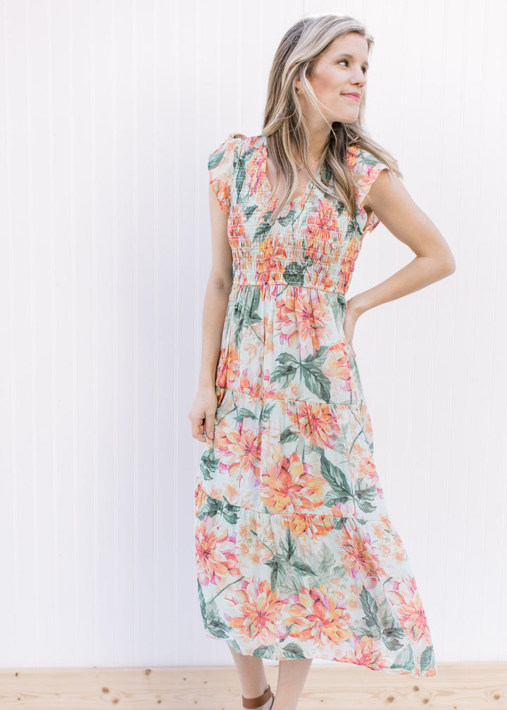 Model wearing a pale green midi with a floral pattern, smocked bodice and cap flutter sleeves. 